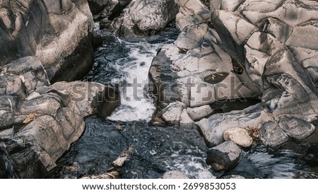 A stream of water flows between large rocks. The water is clear and calm, and the rocks are jagged and rough. The scene is peaceful and serene