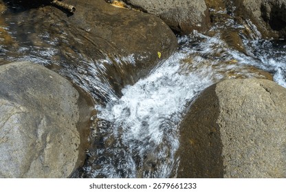 A stream of water flows between two large rocks. The water is clear and calm, and the rocks are large and jagged. The scene is peaceful and serene