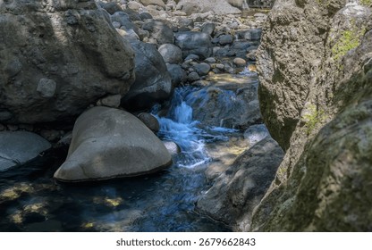 A stream of water flows between two large rocks. The water is clear and calm, and the rocks are large and jagged. The scene is peaceful and serene