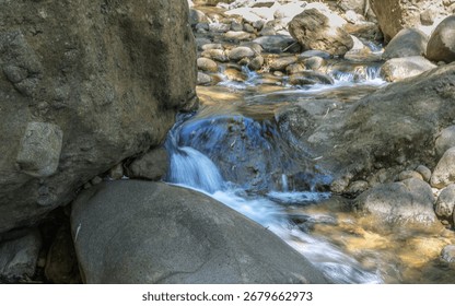 A stream of water flows between two large rocks. The water is clear and calm, and the rocks are large and jagged. The scene is peaceful and serene