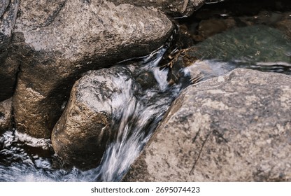 A stream of water flows between two large rocks. The water is clear and calm, and the rocks are rough and jagged. The scene is peaceful and serene