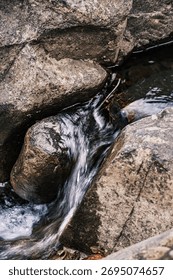 A stream of water flows between two large rocks. The water is clear and calm, and the rocks are rough and jagged. The scene is peaceful and serene