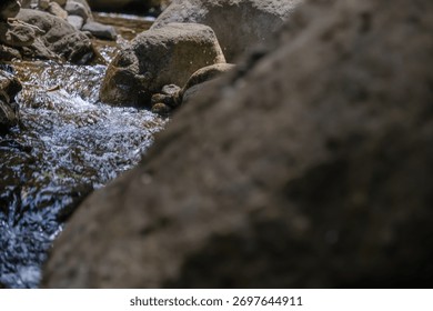 A stream of water flows between two large rocks. The water is clear and the rocks are grey