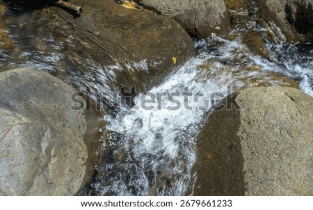 A stream of water flows between two large rocks. The water is clear and calm, and the rocks are large and jagged. The scene is peaceful and serene