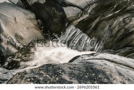 A stream of water flows down a rocky hillside. The water is clear and calm, and the rocks are jagged and rough. The scene is peaceful and serene, with the sound of the water