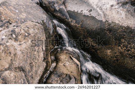 A stream of water flows down a rocky hillside. The water is crystal clear and the rocks are jagged and rough. The scene is peaceful and serene