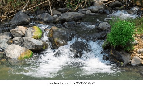 A stream of water flows over a rocky bed. The water is clear and the rocks are large - Powered by Shutterstock