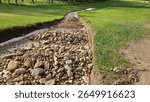 Streambed lined with stones on golf course after rainfall enhances natural drainage in lush green landscape