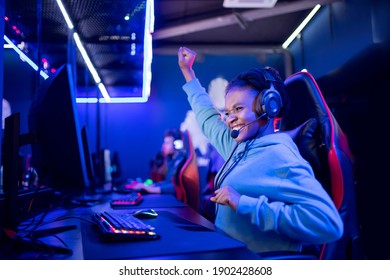 Streamer african young woman rejoices in victory professional gamer playing online games computer with headphones, neon color.