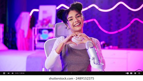 Streamer, portrait and woman with microphone, heart hands and neon light and happy influencer in home studio. Love, emoji and content creator girl in video live stream for like, subscribe and follow - Powered by Shutterstock