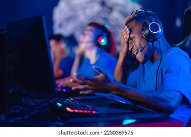 Streamer young african man is defeated in tournament professional gamer playing online games computer with headphones, neon colour, soft focus.