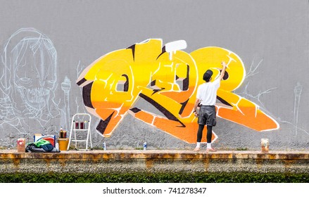 Street artist painting colored graffiti on public space wall - Modern art concept of urban guy performing and preparing live murales paint with yellow aerosol color spray - Cloudy afternoon filter