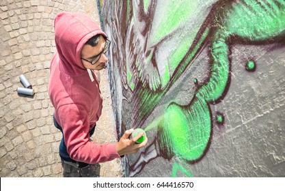 Street artist painting colorful graffiti on generic wall - Modern art concept with urban guy performing and preparing live murales with green aerosol color spray - Sunny afternoon neutral filter - Powered by Shutterstock