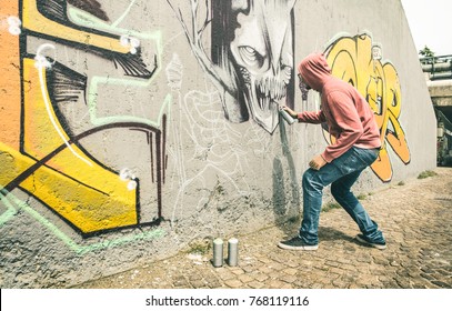 Street artist painting colorful graffiti on generic wall - Modern art concept with urban guy performing and preparing live murales with multi color aerosol spray - Contrast retro vintage filter