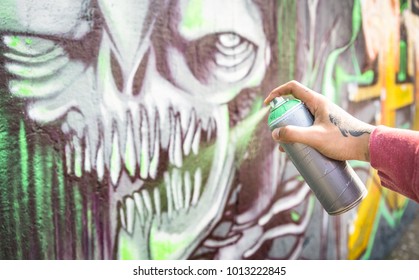 Street artist painting colorful monster graffiti on public wall - Modern art concept with urban guy performing and preparing live murales with multi color aerosol spray - Focus on hand 