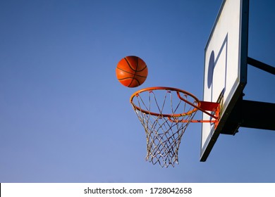 Street basketball ball falling into the hoop. Close up of orange ball above the hoop net with blue sky in the background. Concept of success, scoring points and winning. Copy space - Powered by Shutterstock