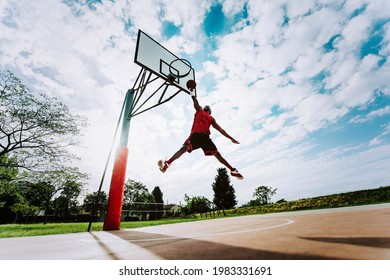 Street Basketball Player Making A Powerful Slam Dunk On The Court - Athletic Male Training Outdoor At Sunset - Sport And Competition Concept