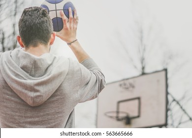 Street Basketball Player Shooting Hoops At The Basketball Court Outdoor - Back View Of A Young Man Playing Basket With A Blue And White Ball Making A Score - Sport And People Concept