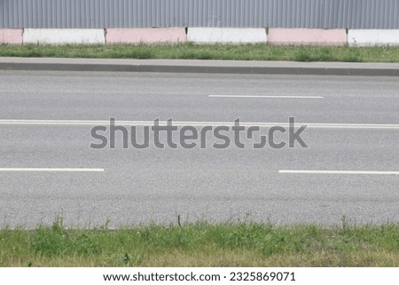 A street border painted in white and black on the background of the road and green foliage in the summer closeup. Road safety, minimalism