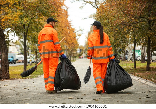 Street cleaner with brooms and garbage bags outdoors\
on autumn day, back view