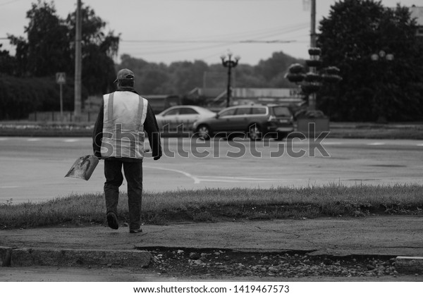 Street cleaner going to work on street in early\
morning. Laborer goes towards roadway. Janitor with shovel dressed\
in worker vest. Russia.