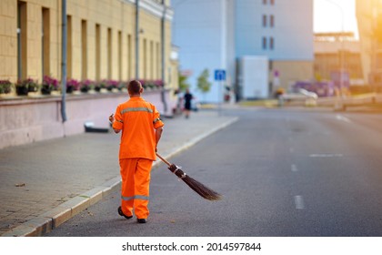 Street cleaner sweeping road and pedestrian zone in evening. Municipal worker sweep road with broomstick and collects garbage. Sanitation worker clean up street. Utility worker cleaning city street