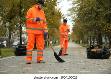 Street cleaners sweeping fallen leaves outdoors on autumn day
