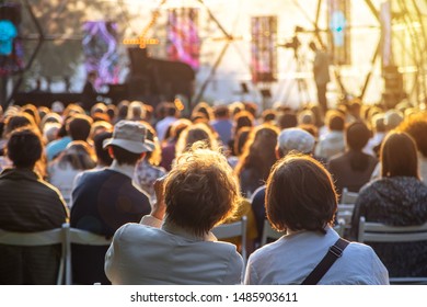 Street Concert In The Park In Summer Backs Of Spectators Sitting On Chairs At The Stage