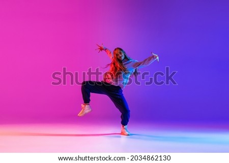 Street dance style. Young beautiful female hip-hop dancer dancing isolated on neon background. Sport achievement, spirit of expression. Concept of dance, youth, hobby, dynamics, movement, action, ad