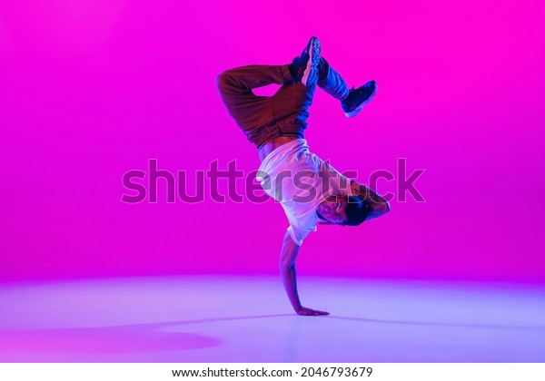 Street dance style. Young stylish man, hip-hop\
dancer dancing in modern clothes isolated over bright magenta\
background at dance hall in neon light. Youth culture, moves and\
fashion, action.