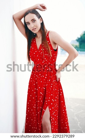Street fashion: beautiful sweet girl in red dress. Portrait of alluring young woman standing at the wall