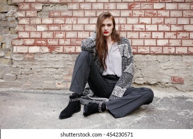 Street Fashion Concept - Portrait Of A Pretty Female. Wearing Grey Coat, Trousers Straight Cut And Black Leather Ankle Boots. Beautiful Autumn Woman With Red Lips. Vogue Style. 