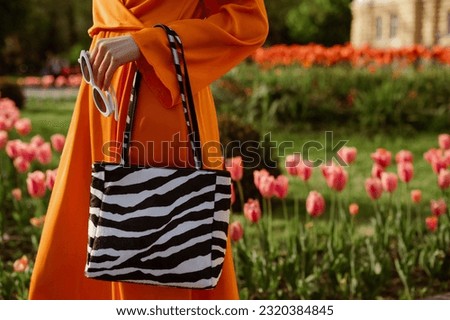 Street fashion details: woman wearing trendy orange dress, holding sunglasses, zebra print leather bag, handbag. Copy, empty space for text