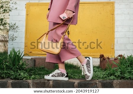 Street fashion elements: woman wearing trendy outfit with pink suit, zebra print sneakers, holding yellow faux leather handbag. Copy, empty space for text