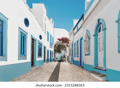 Street in fishermen village with white and blue houses and typical Portuguese pavement in Olhao, Algarve region - Popular travel destinations in Portugal