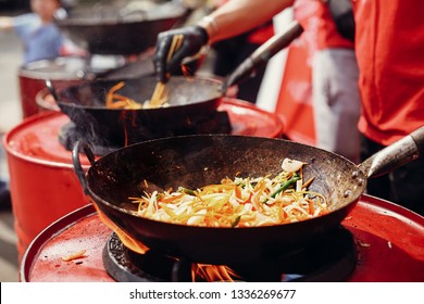 Street food chef cooking noodles and vegetables in a pan on fire at open kitchen. Fried noodles in a wok on the open fire. Asian street food festival in city - Powered by Shutterstock