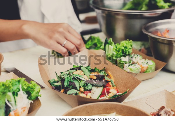 Street food festival, catering service. Vegetable\
salads in kraft paper plates sold outdoors at local market place,\
shallow depth of field