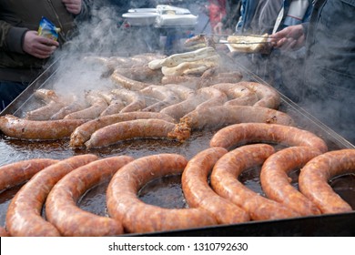 Street Food Market Vendor Cooking and Selling Sausages. Tasty Sausages on Large Commercial Griddle Hotplate. Street Food Cooking on Big Frying Pan Outdoor. Tongs In Hand Holding Sausages.
