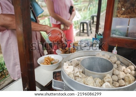 A Street Food Vendor Preparing Mouthwatering Indonesian Authentic Bakwan Malang on a Pushcart with a Female Buyer on the Background