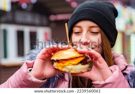 Street food. young woman holding juicy burger and eating oudoor winter