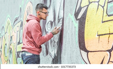 Street graffiti artist painting with a color spray can a dark monster skull graffiti on the wall in the city- Urban, lifestyle street art concept - Main focus on his hand