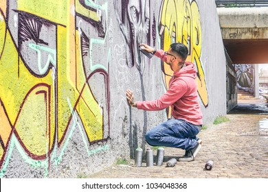 Street graffiti artist painting with a color spray can a dark monster skull graffiti on the wall in the city outdoor - Urban, lifestyle contemporary street art concept - Main focus on his hand