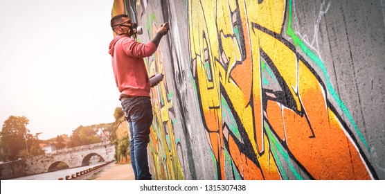 Street graffiti artist painting with a color spray can a dark monster skull graffiti on the wall in the city- Urban, lifestyle street art concept 