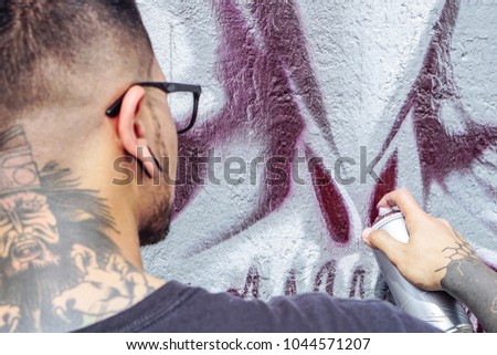 Street graffiti artist painting with a color spray can a dark monster skull graffiti on the wall in the city outdoor - Close up hand paints - Urban, lifestyle contemporary street art concept 