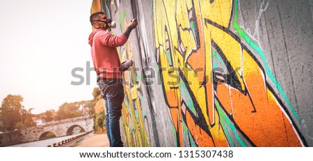 Street graffiti artist painting with a color spray can a dark monster skull graffiti on the wall in the city- Urban, lifestyle street art concept 