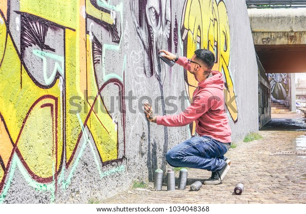 Street graffiti artist painting with a color spray\
can a dark monster skull graffiti on the wall in the city outdoor -\
Urban, lifestyle contemporary street art concept - Main focus on\
his hand