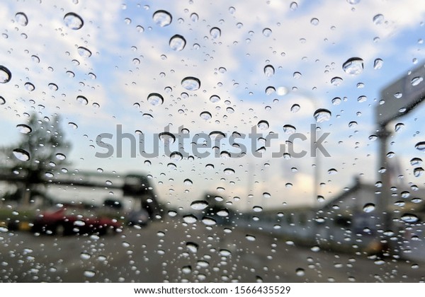Street in the heavy rain. Water drops or rain\
in front of mirror of car on road or street. Driving in rain.\
Blurred background.