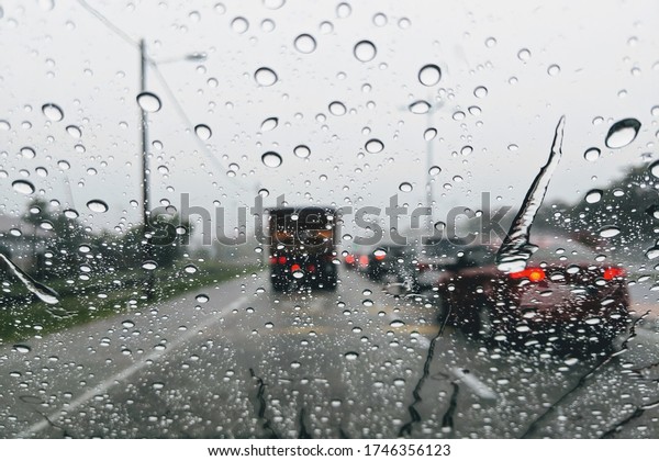 Street in the heavy rain. Water drops or rain\
in front of mirror of car on road or street. Driving in rain.\
Blurred background.