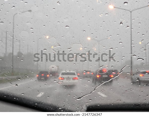 \
\
Street in the heavy rain. Water drops or\
rain in front of mirror of car on road or street. Driving in rain.\
Blurred background.