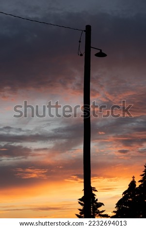 A street lamp on an old wooden telephone pole silhouette under a sunset sky background in Alberta Canada.